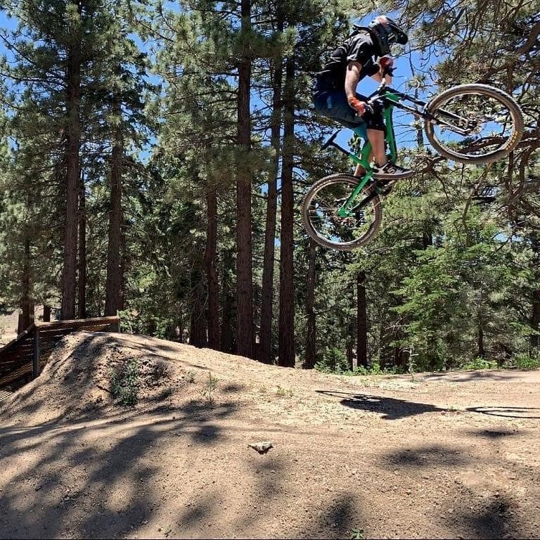 A rider throwing the back wheel out sideways over a dirt jump, tall pines behind